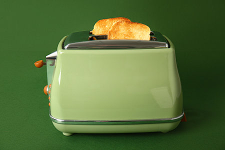 Modern toaster with crispy bread slices on green background