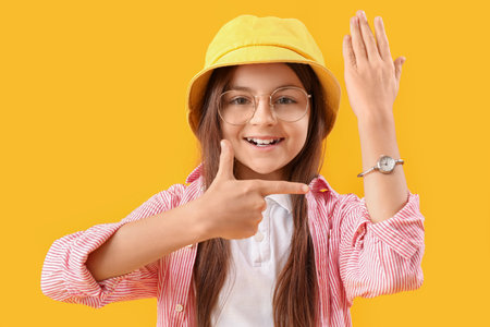 Little girl pointing at wristwatch on yellow backgroundの写真素材