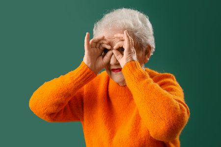 Funny senior woman in orange sweater on green backgroundの写真素材