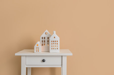 Glowing house candle holders on table near beige wallの写真素材