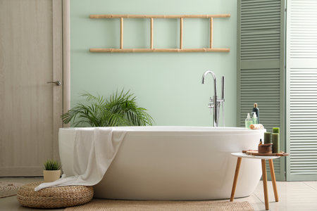 Interior of bathroom with modern bathtub, bath accessories and houseplants near green wallの写真素材