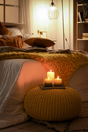 Interior of bedroom with cozy blankets on bed, burning candles and glowing lamp late in the eveningの写真素材