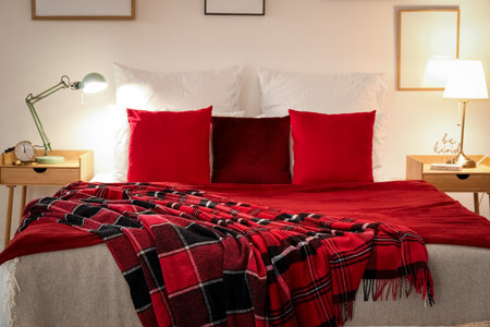 Interior of bedroom with red checkered blankets on bed, blank frames and glowing lamps late in the eveningの写真素材
