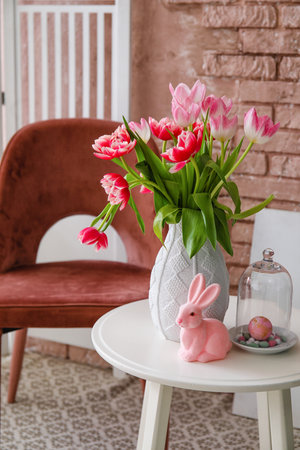 Vase with tulips and Easter bunny on end table and armchair near brick wallの写真素材