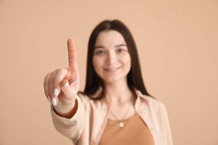 Young woman pointing at something on beige background, closeupの写真素材