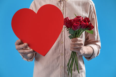 Woman holding heart-shaped gift and roses on blue background. Valentine's Day celebrationの写真素材