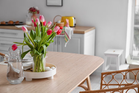 Vase with tulips, Easter eggs and jug of water on dining table in kitchenの写真素材