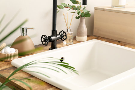 Ceramic sink with bath accessories, reed diffuser and eucalyptus in vase near light wall, closeup