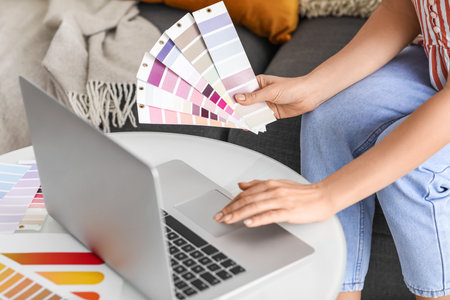 Young woman with paint palette colors using laptop at home, closeupの写真素材