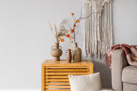 Vases with tree branches, flowers and pampas grass on table near light wall