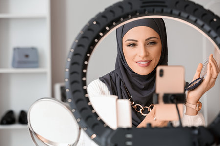 Muslim beauty blogger with makeup brush taking video at homeの写真素材