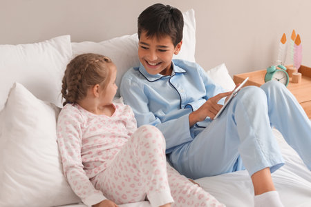 Little boy and his sister watching cartoons on tablet computer in the bedroomの写真素材