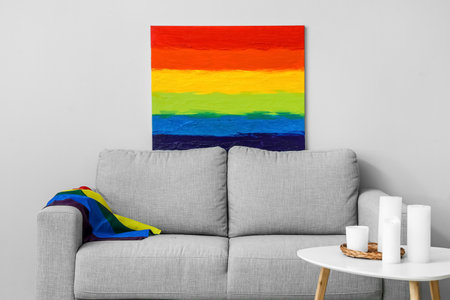 Sofa with LGBT flag, painting and candles on table near light wallの写真素材