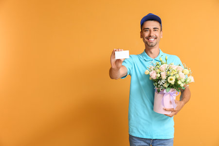 Delivery man with bouquet of flowers and business card on color backgroundの写真素材
