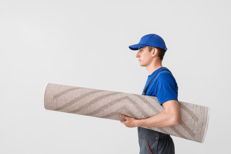 Worker with rolled carpet on white backgroundの写真素材
