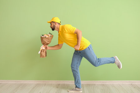 Running delivery man with bouquet of flowers on color backgroundの写真素材