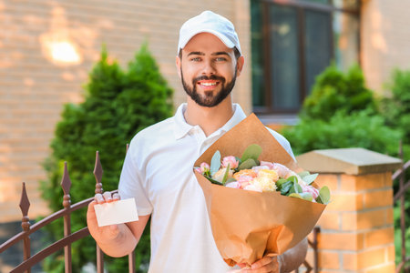 Delivery man with bouquet of beautiful flowers and blank business card outdoorsの写真素材