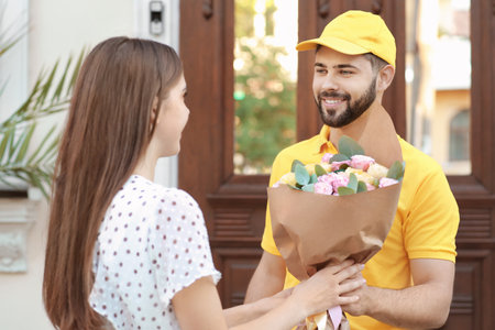 Young woman receiving flowers from courier outdoorsの写真素材