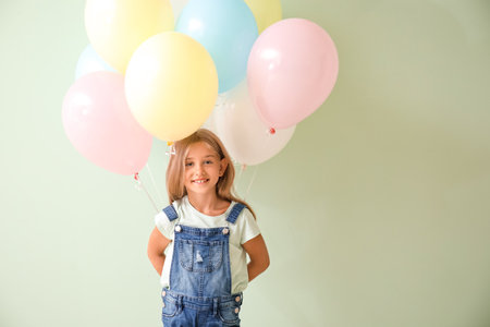 Little girl with balloons on color background