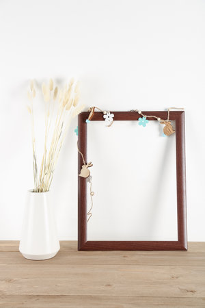 Blank frame with Easter decor and vase with dried flowers on table near white wallの写真素材