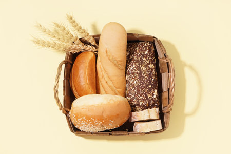Basket with loaves of different bread and wheat ears on yellow backgroundの写真素材