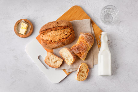 Board with slices of fresh bread and bottle of milk on white backgroundの写真素材