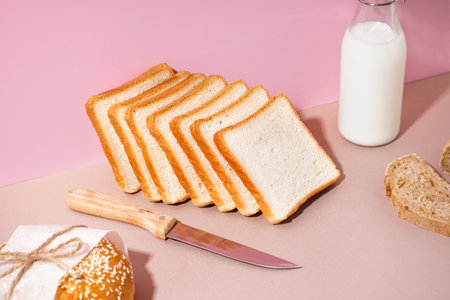 Pieces of fresh bread, knife and bottle of milk on pink background