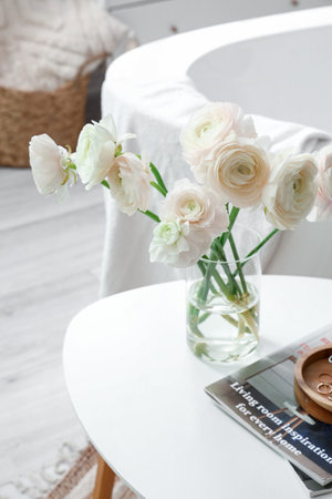Vase with ranunculus flowers and magazines on table in bathroom, closeup
