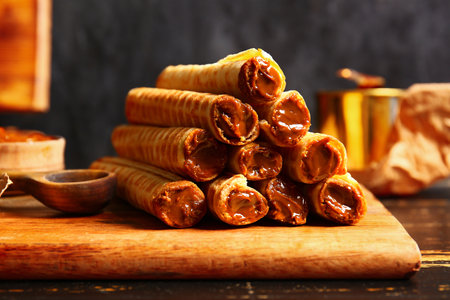 Stack of delicious wafer rolls with boiled condensed milk on black wooden tableの写真素材