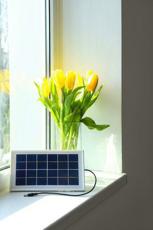 Portable solar panel and vase with tulips on windowsill in roomの写真素材