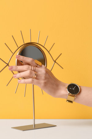 Woman with golden wristwatch and mirror on table near yellow wallの写真素材