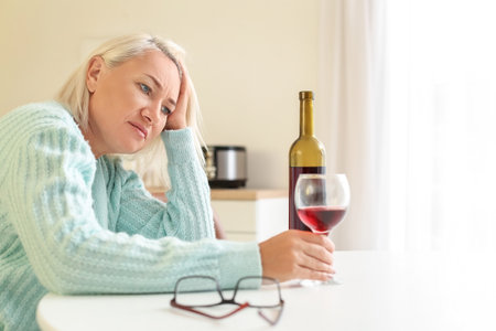 Stressed mature woman drinking wine at homeの写真素材
