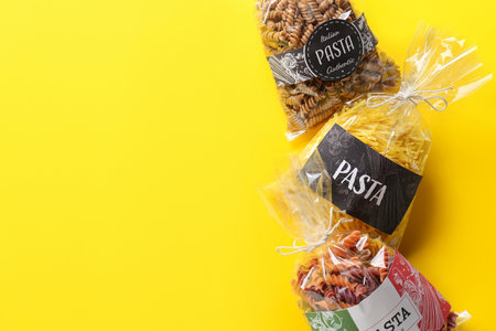 Bags with uncooked pasta on color background