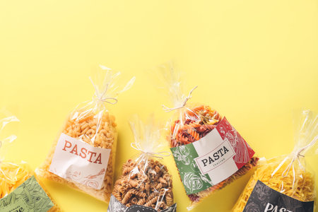 Bags with uncooked pasta on color background