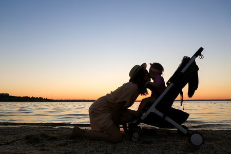 Silhouette of woman and her cute baby in stroller near river at sunsetの写真素材