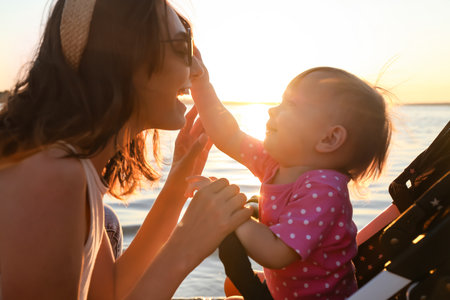 Woman and her cute baby in stroller near riverの写真素材