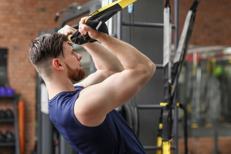 Handsome muscular man exercising with TRX straps in gymの写真素材