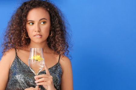 Young African-American woman with beautiful eyeshadows and glass of water on color backgroundの写真素材