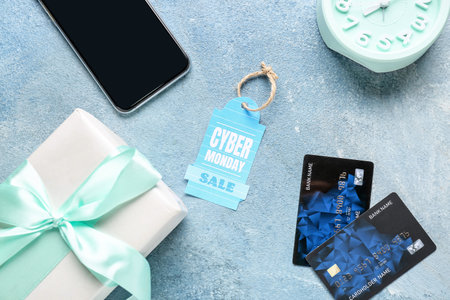 Gift box with credit cards, mobile phone, alarm clock and shopping tag with text CYBER MONDAY SALE on color backgroundの写真素材