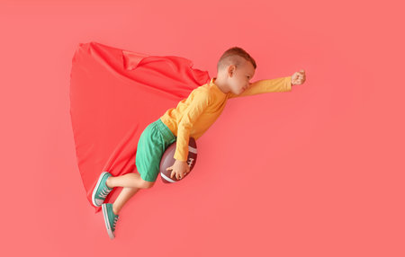 Little boy with rugby ball and cloak on color backgroundの写真素材