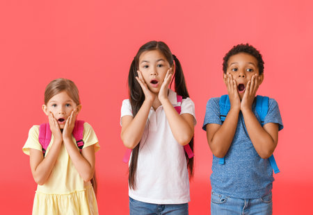 Surprised little schoolchildren on color background