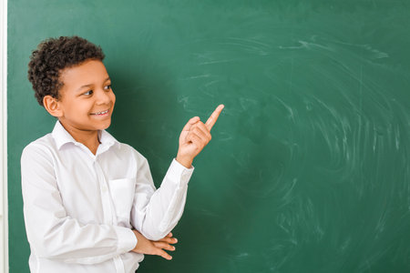 Little African-American schoolboy showing something near chalkboard in classroomの写真素材