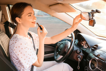 Beautiful woman applying lipstick in modern carの写真素材