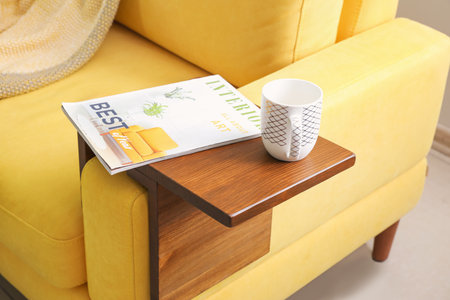 Cup of tea and magazine on armrest table in roomの写真素材