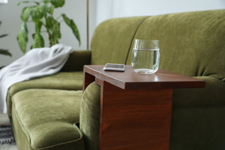 Glass of water with mobile phone on armrest table in roomの写真素材