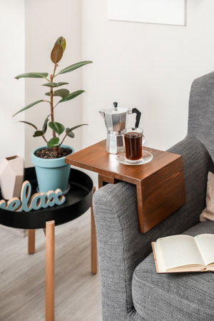 Cup of drink and coffee pot on armrest table in roomの写真素材