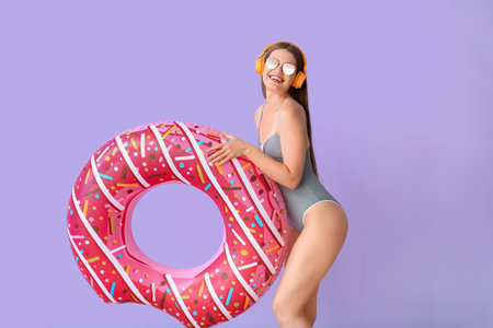Young woman with headphones and inflatable ring on color backgroundの写真素材