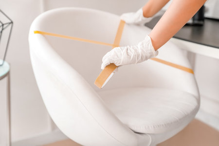 Female makeup artist applying a marking tape on client's armchair in salon during coronavirus epidemicの写真素材