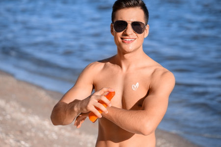 Handsome young man applying sunscreen cream on sea beachの写真素材