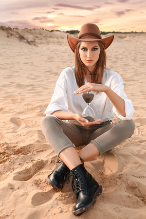 Beautiful fashionable young woman with hourglass in desertの写真素材